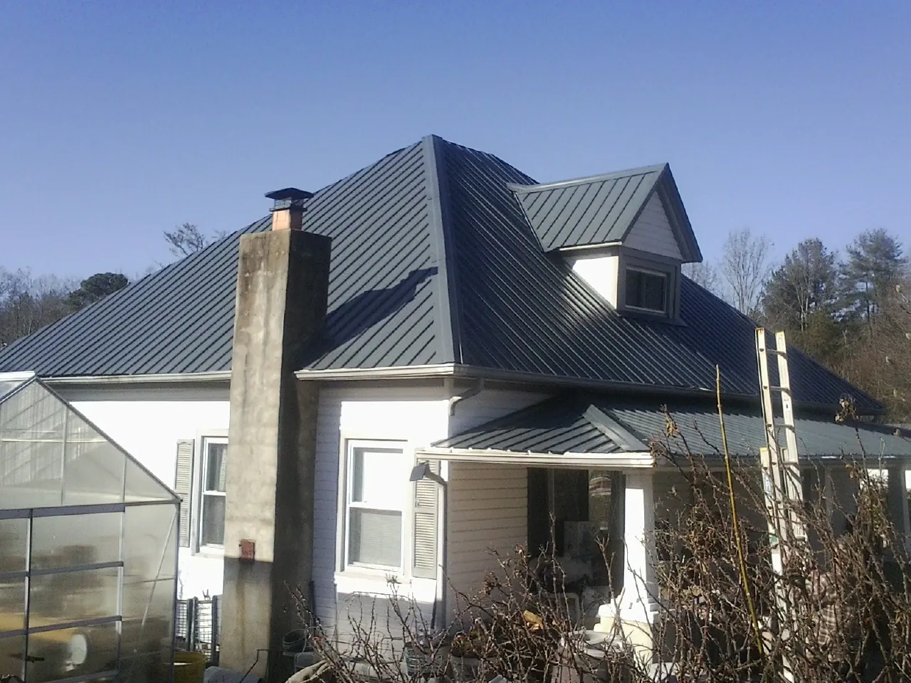 Dark blue standing seam metal roof on a white farmhouse with dormer — Slate & Tile Roof Repair by Roofing Brothers in Dent