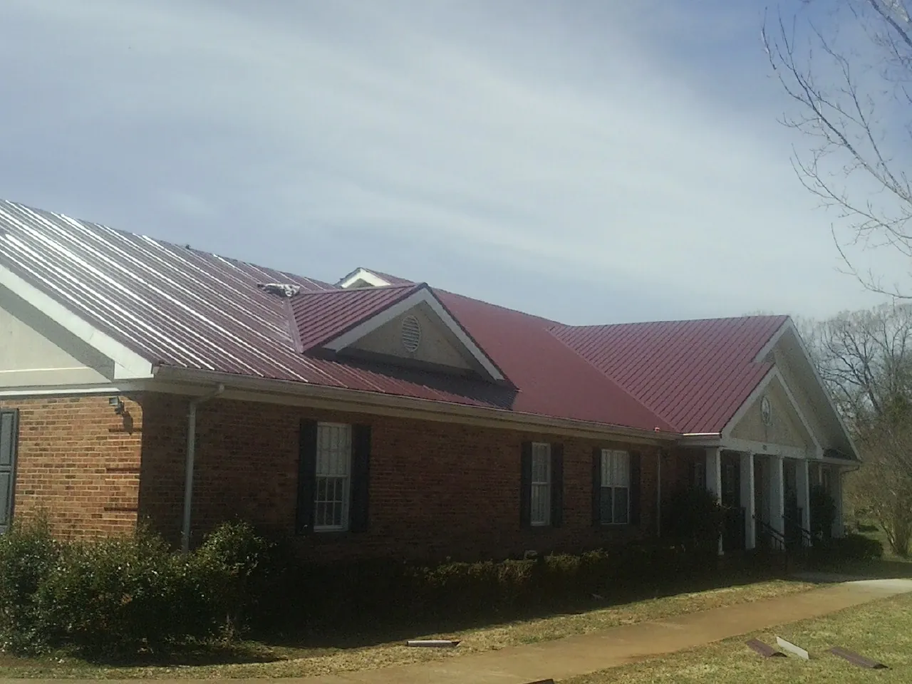 Red metal roof with gabled entries on a long brick building, from a Hail Damage Roof Repair job in Dent