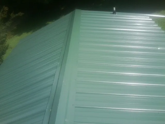 New green metal panels meeting at the ridge of a roof — Flat Roof Repair work by our crew in Dent