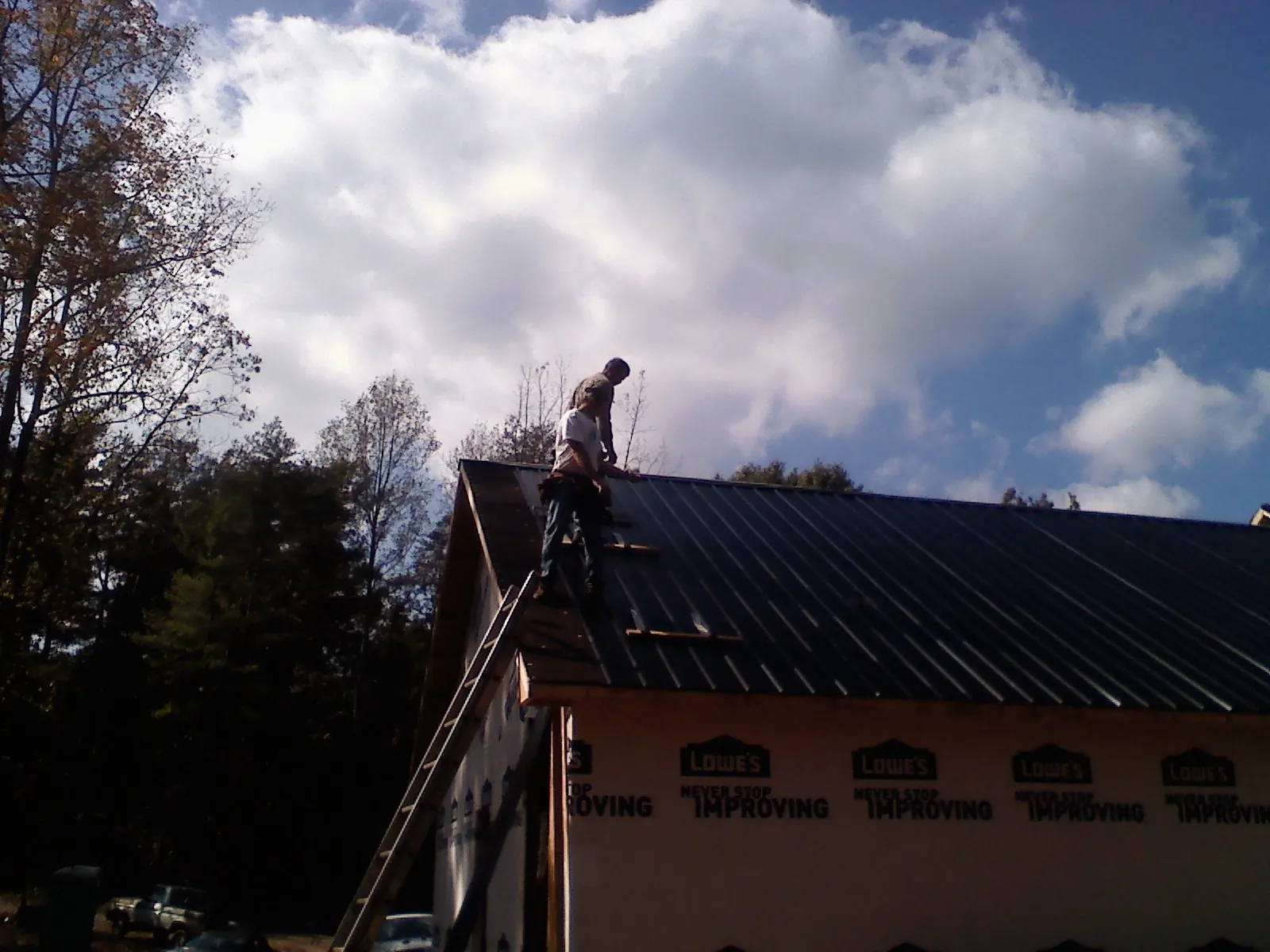 Roofer fastening dark metal panels high against a cloudy sky, from a Roof Inspection job in Dent